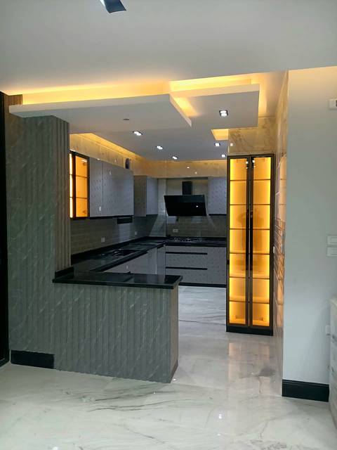 Grey kitchen with a black stone worktop and a lit glass cabinet